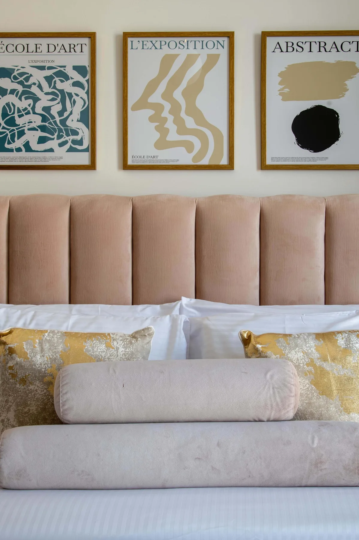 Un dormitorio con la cama tendida, cojines decorativos y cuadros enmarcados sobre el cabecero.