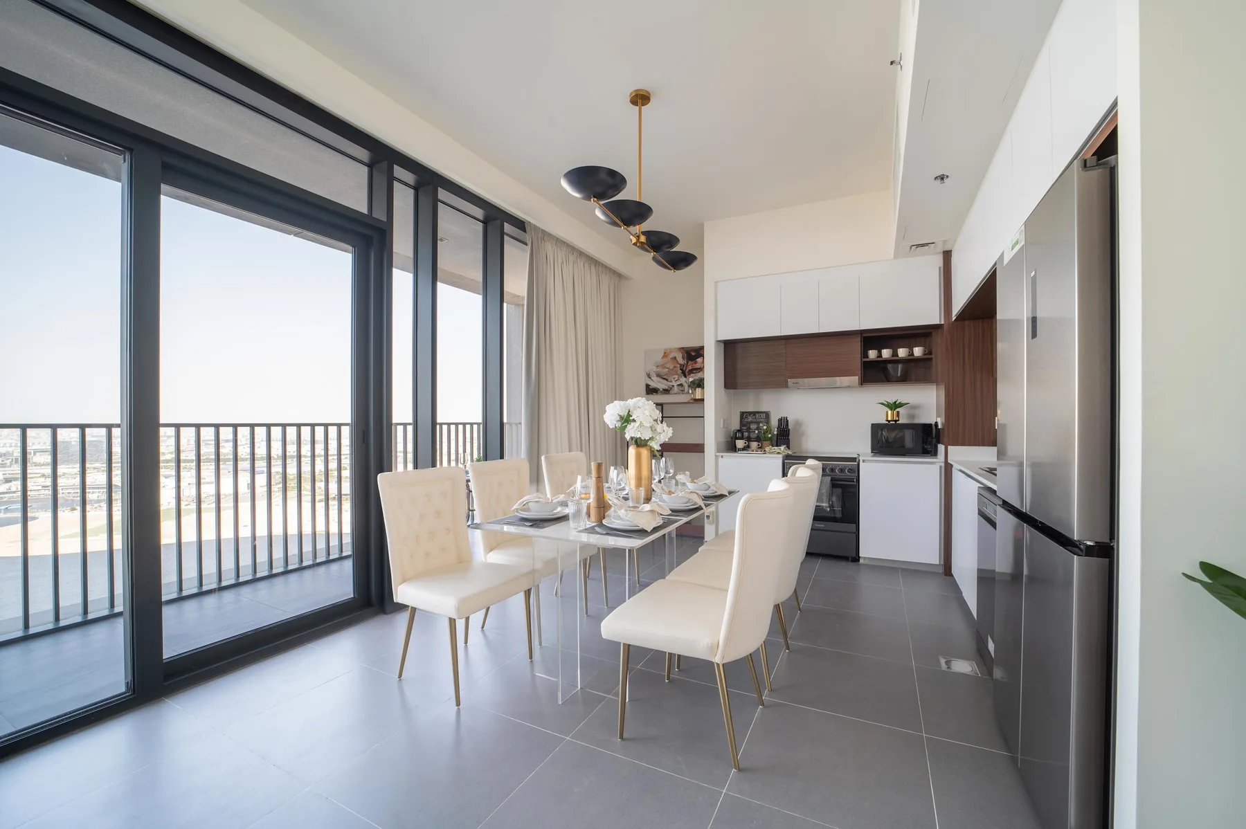 Un comedor luminoso junto a una cocina moderna, con grandes puertas de vidrio hacia un balcón.