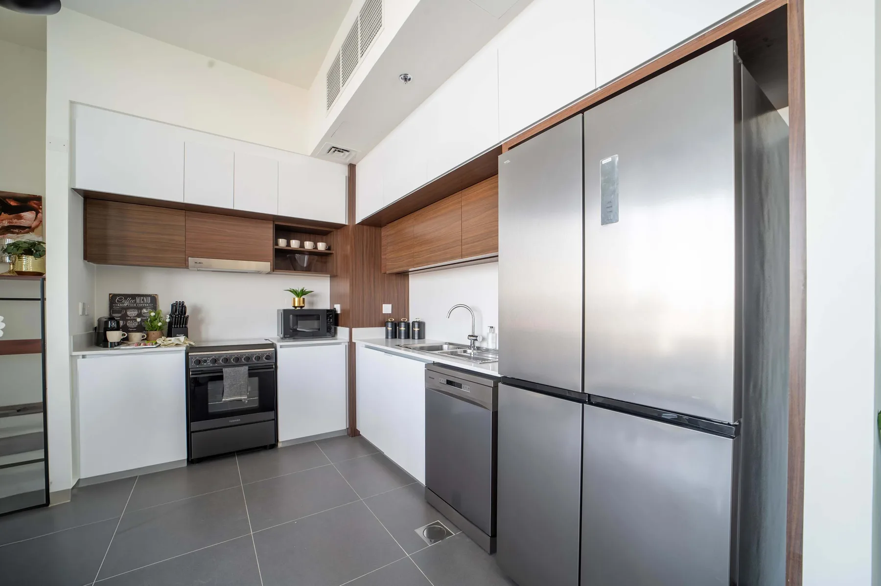 Una cocina moderna con gabinetes blancos, detalles de madera y electrodomésticos de acero inoxidable.