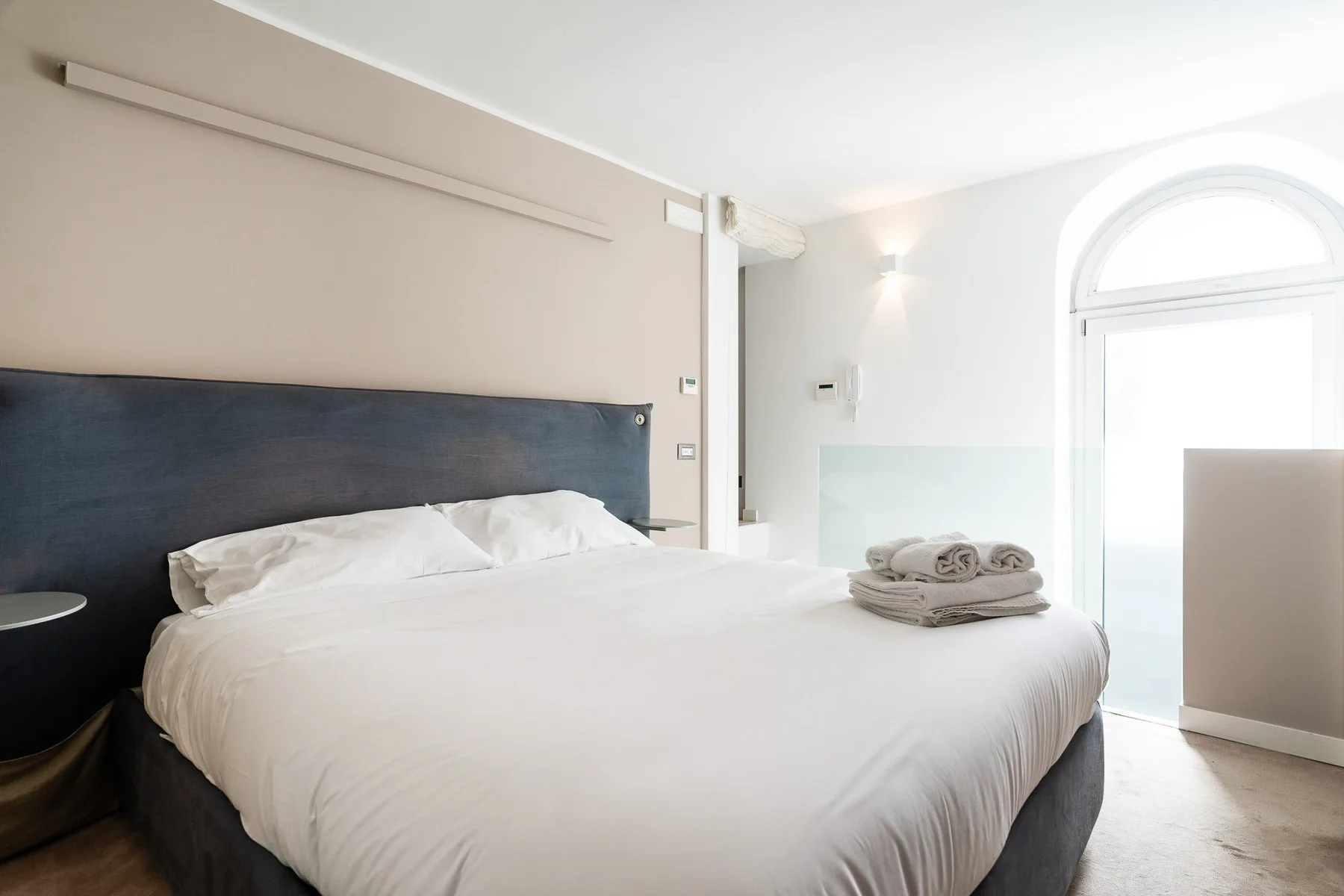 Un dormitorio luminoso con una cama grande y toallas dobladas junto a la ventana.