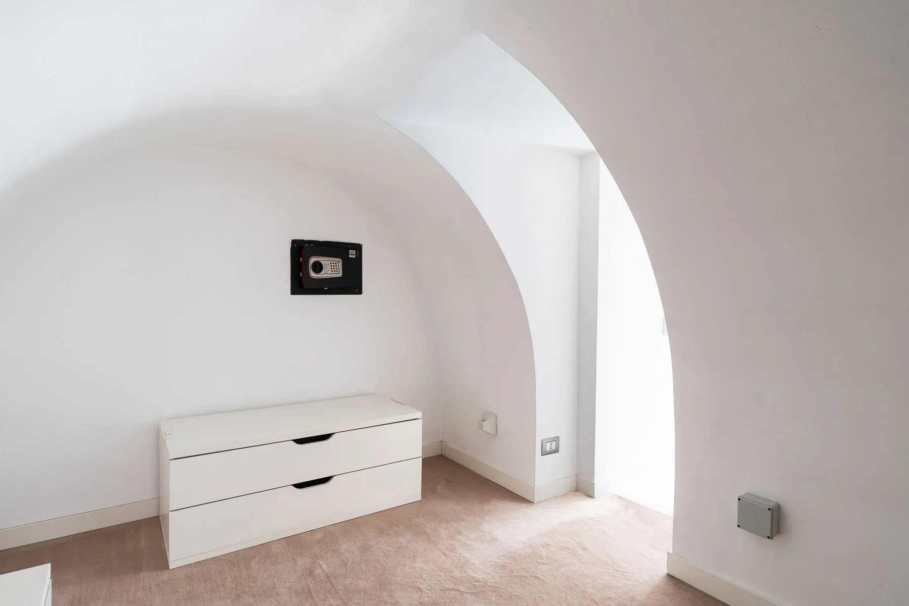 Una habitación blanca y luminosa con paredes curvas, un mueble bajo con cajones y un arco.