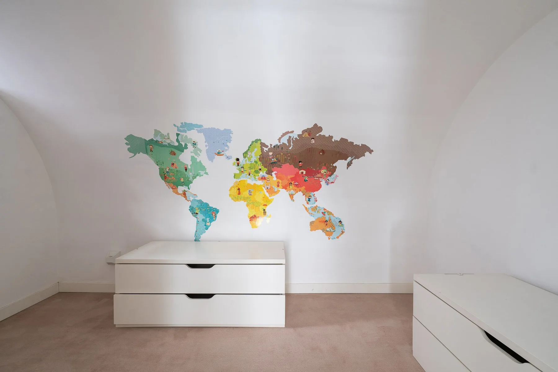 Una habitación luminosa con un mapa mundi colorido sobre cajones blancos.