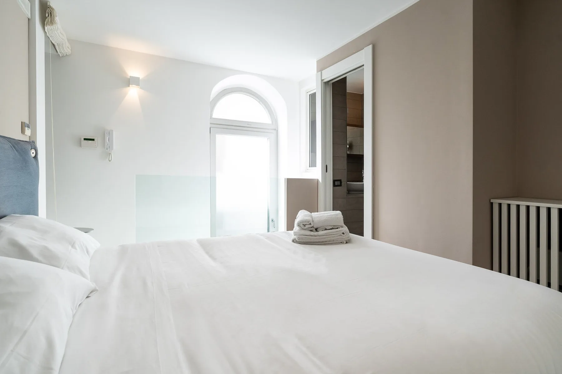 Un dormitorio luminoso con ropa de cama blanca y una ventana arqueada.