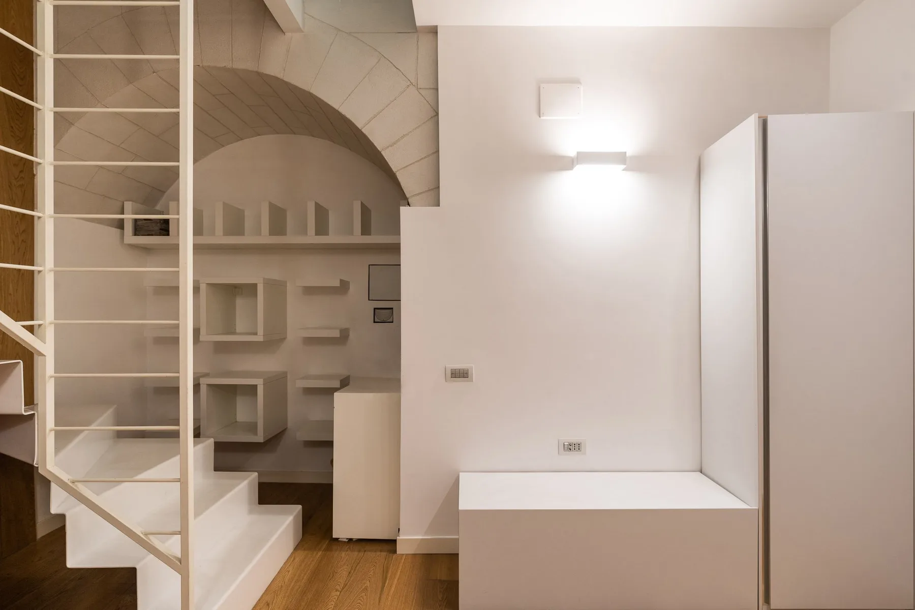 Interior moderno con escalera, estanterías empotradas y una cama blanca.