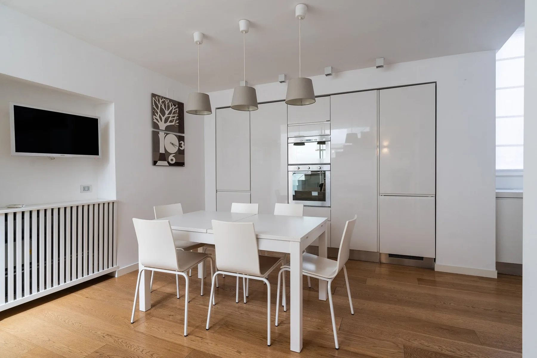 Un comedor luminoso con una mesa blanca y sillas junto a armarios empotrados.