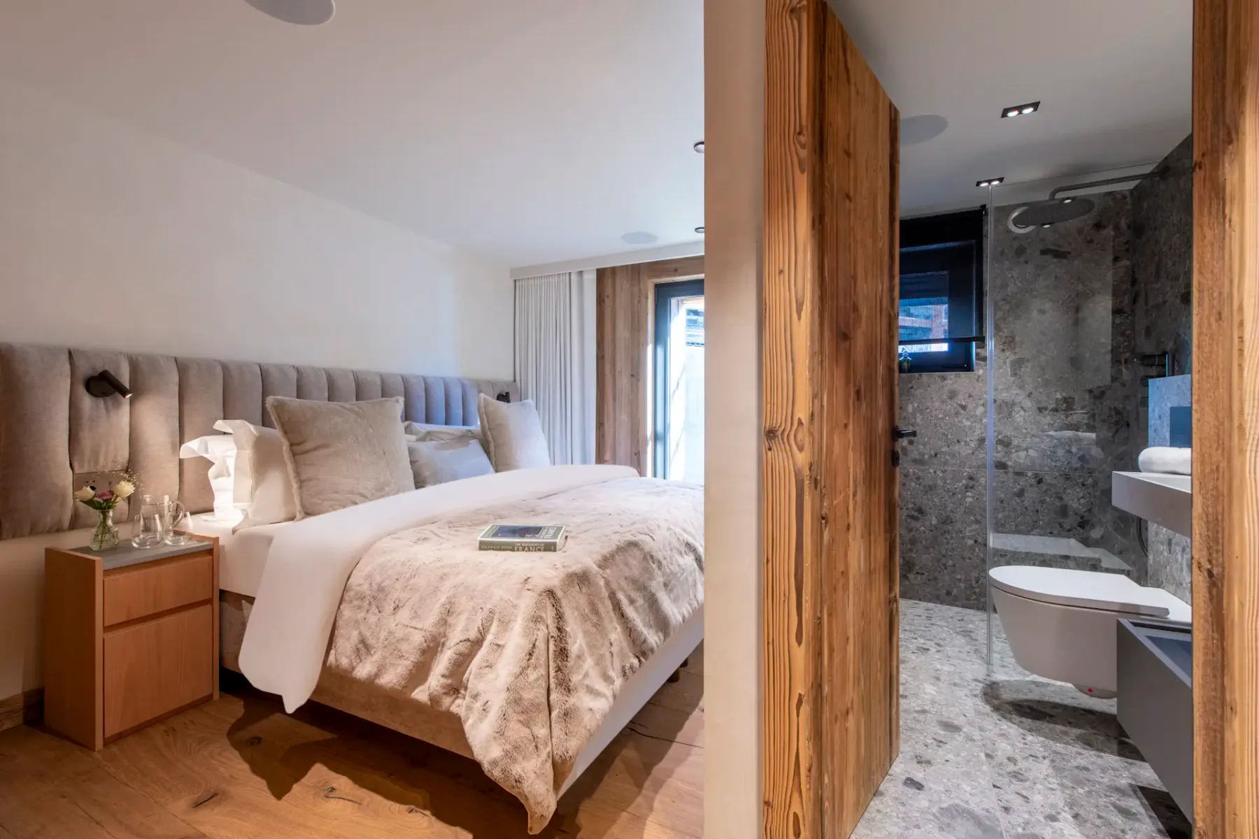 A cozy bedroom with a wooden accent wall, plush bedding, wall-mounted lamps, and a book titled