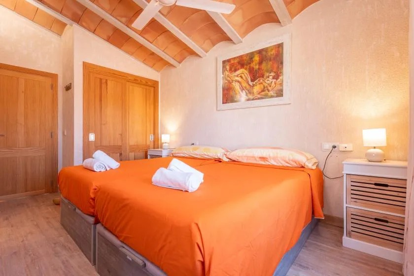 Un dormitorio con ropa de cama naranja, puertas de madera y un cuadro en la pared.
