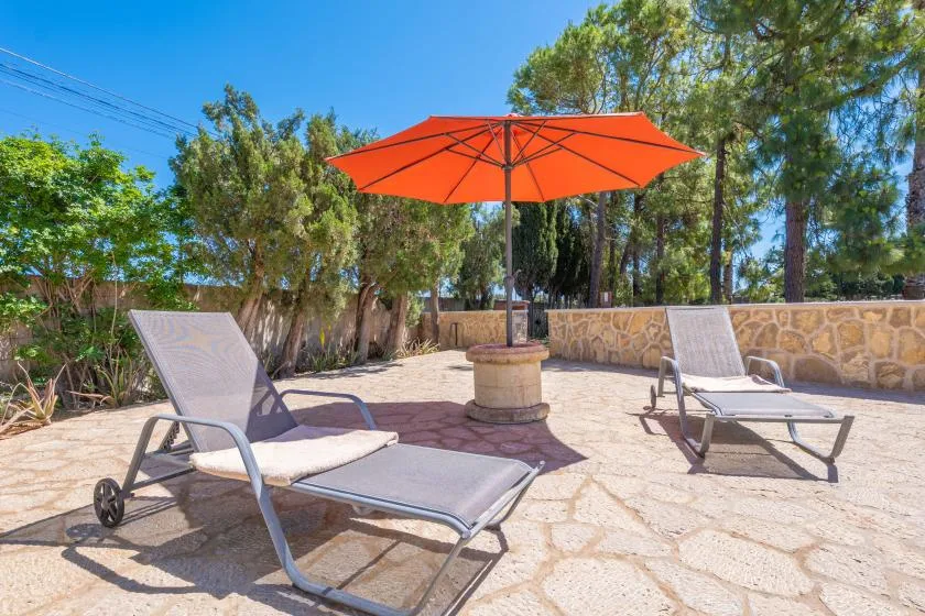 Un patio al aire libre con asientos reclinables bajo una sombrilla naranja.