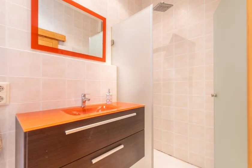 Un baño alicatado con un tocador naranja y una mampara de ducha de vidrio.