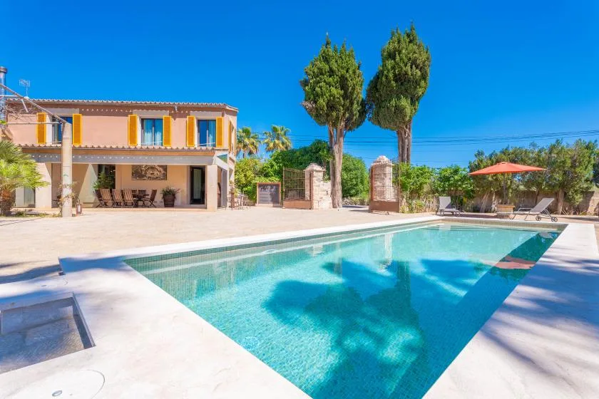 Una piscina junto a una casa de dos plantas y asientos al aire libre.