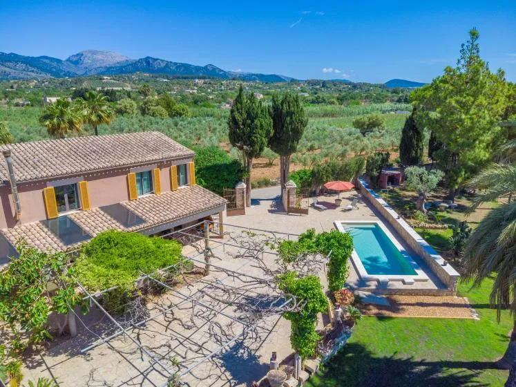 Una casa rural y una piscina exterior están rodeadas de campos verdes, con montañas al fondo.