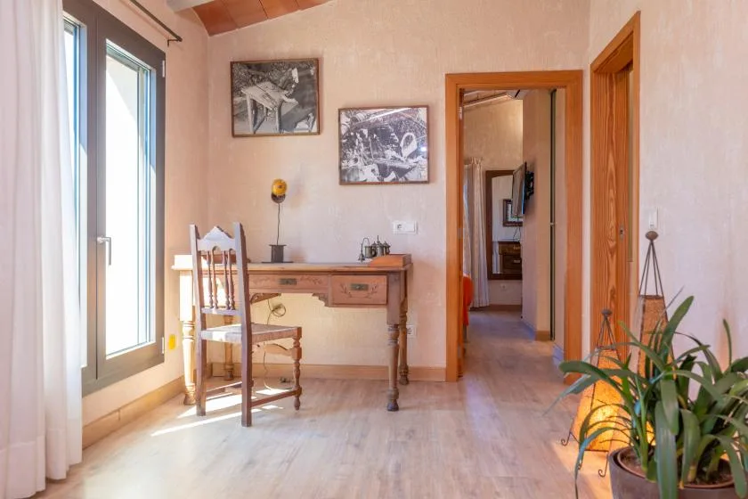 Una habitación luminosa con un escritorio de madera junto a ventanas altas y cuadros enmarcados.