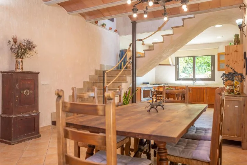 Un cálido comedor con una gran mesa de madera bajo una escalera abierta.