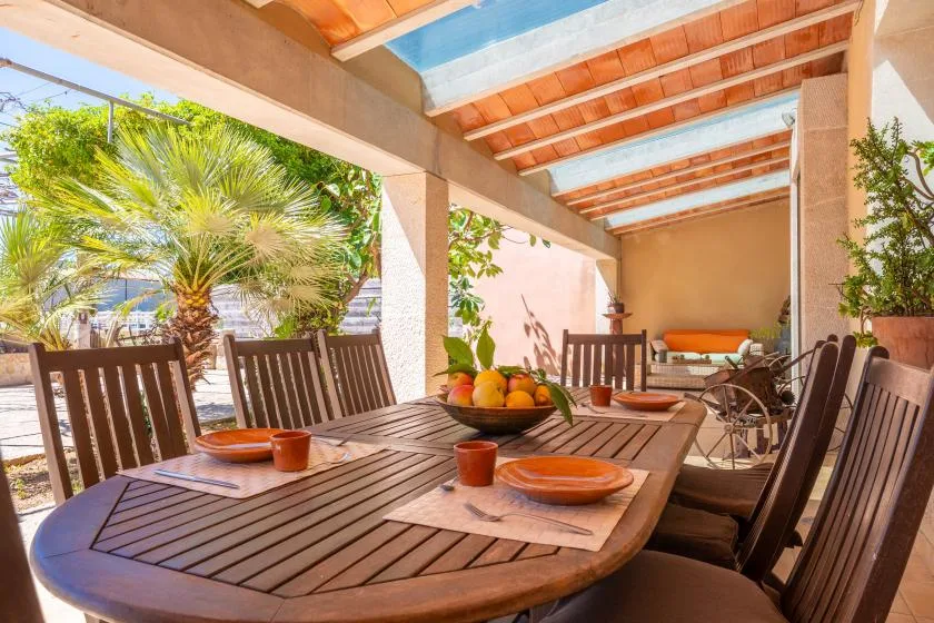 Un comedor exterior cubierto tiene una mesa grande de madera y asientos alrededor.