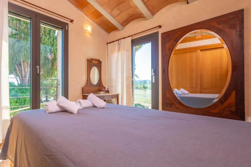 Un dormitorio con una cama, ventanas altas y una ventana interior redonda.