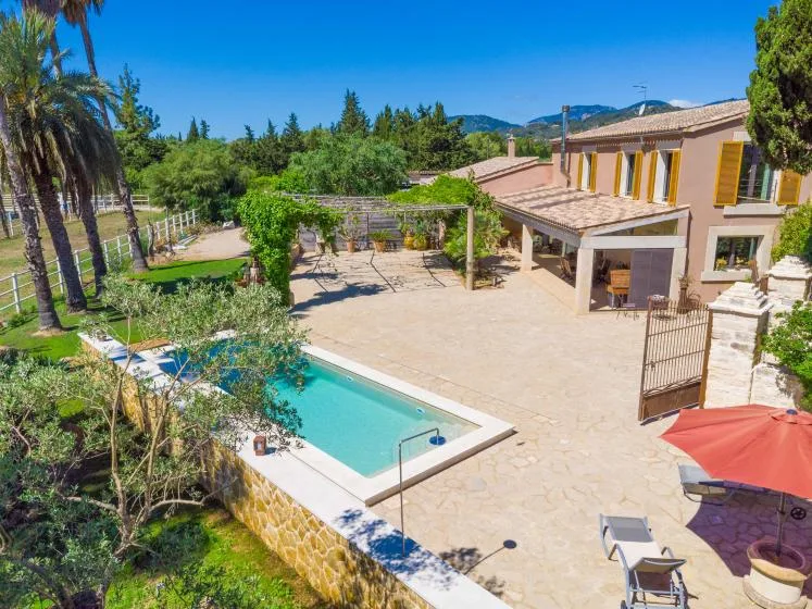 Una piscina al aire libre y un patio pavimentado junto a una casa de dos plantas.