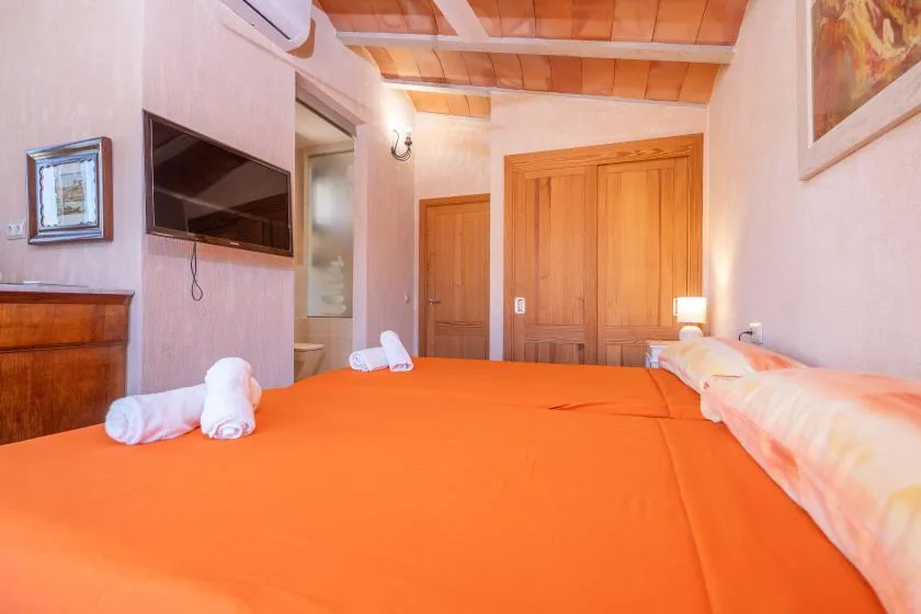 Un dormitorio con ropa de cama naranja, puertas de madera y un televisor en la pared.