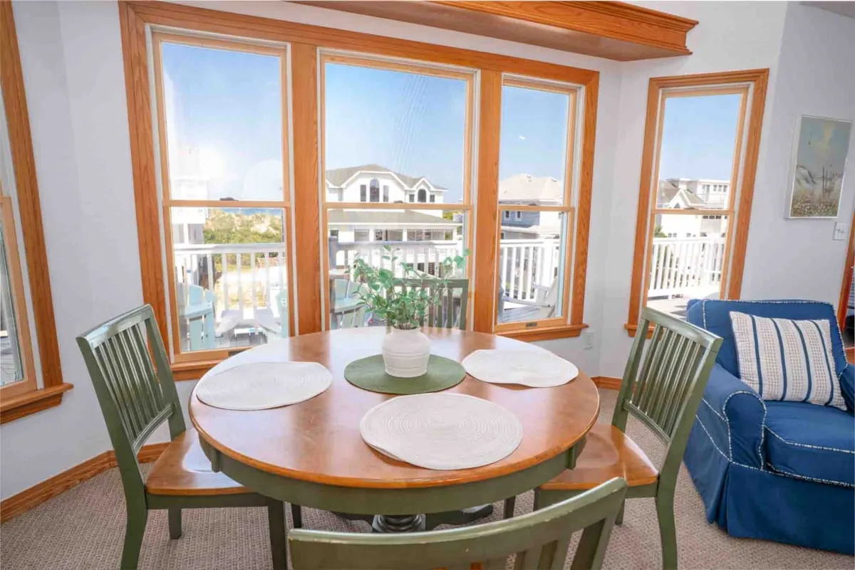 Comedor con una mesa redonda de madera junto a grandes ventanas.