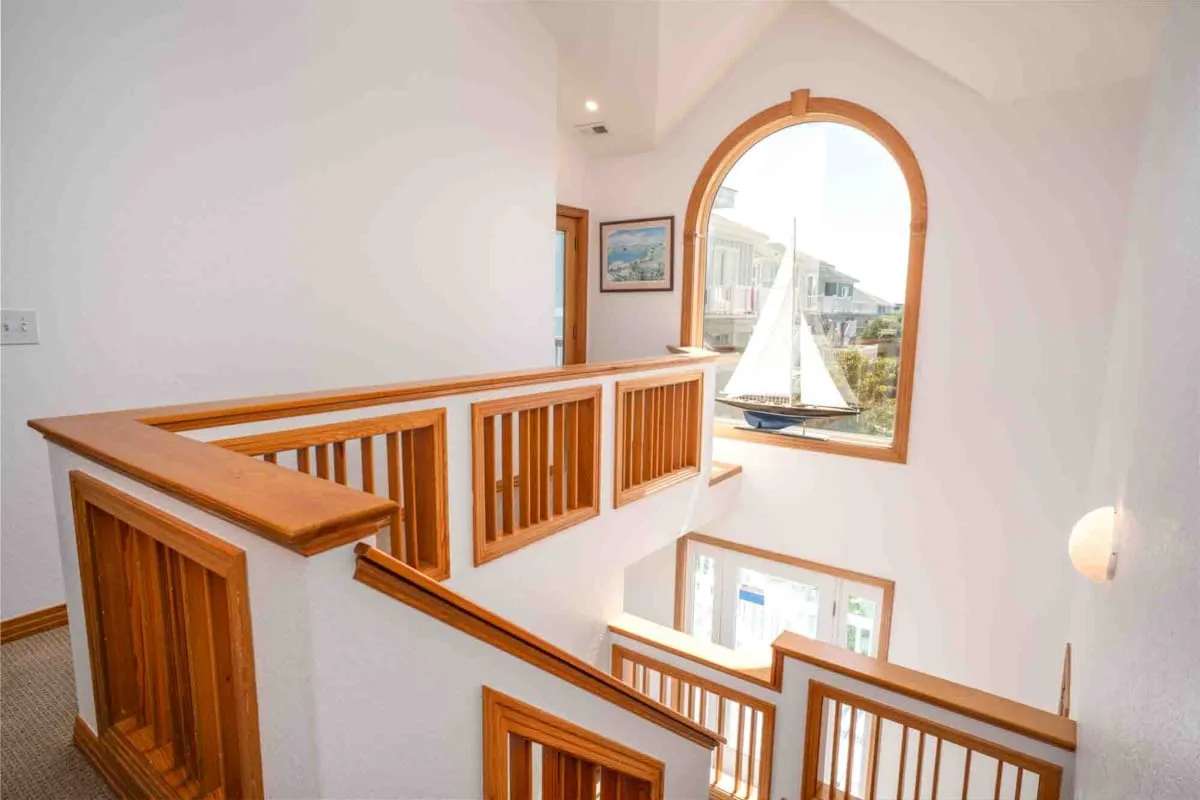 Un descansillo interior luminoso tiene barandillas de madera y una ventana arqueada con vistas a un velero.
