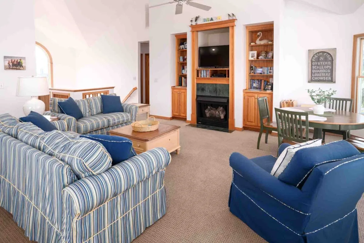 Una sala de estar con asientos a rayas, sillones azules y un mueble de madera para televisión.