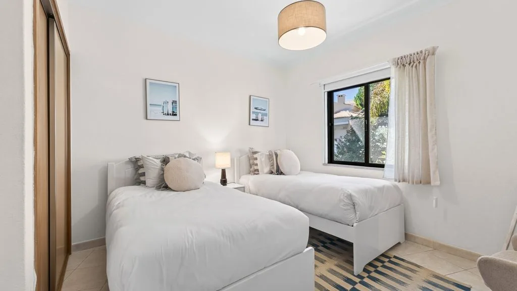 A bright bedroom with white bedding and a window overlooking greenery.