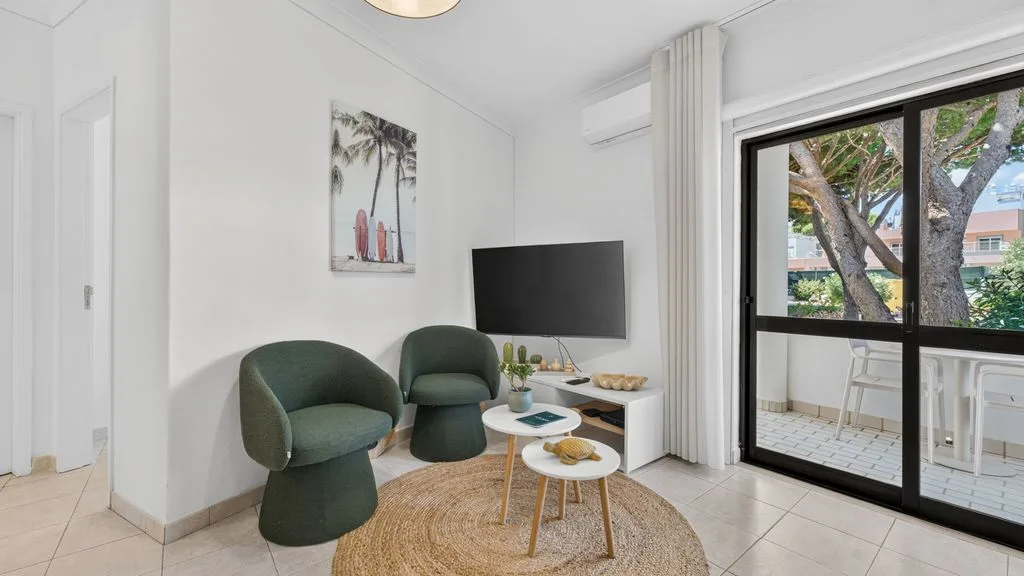 A bright living room with green seating, a television, and a glass door to a balcony.