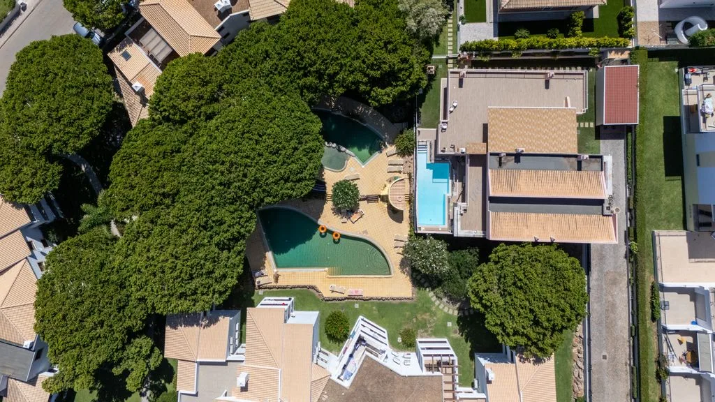 An aerial view shows a residential complex surrounded by trees, with a swimming pool.