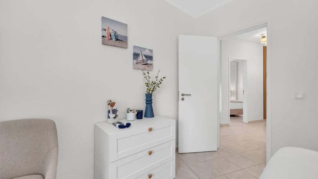 A bright bedroom with a white chest of drawers and an open doorway.