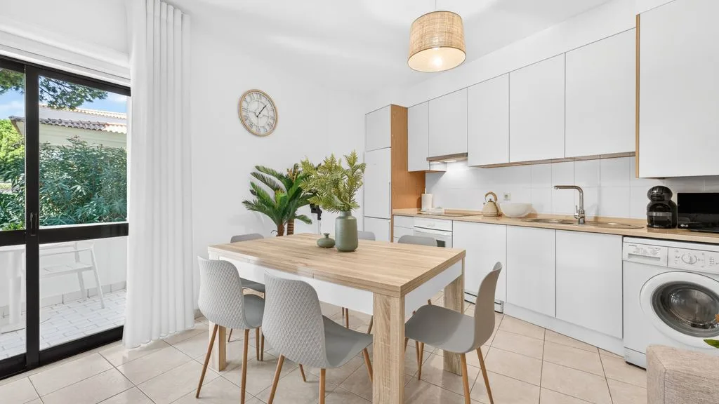 A bright dining area with a wooden table beside a modern kitchen.