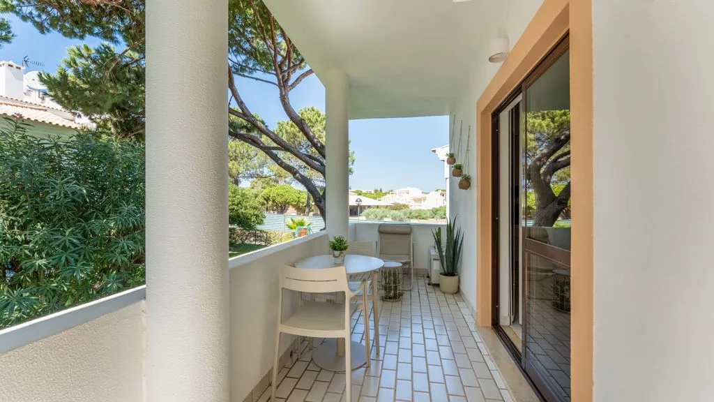 A covered balcony with a small table and seating overlooks greenery.