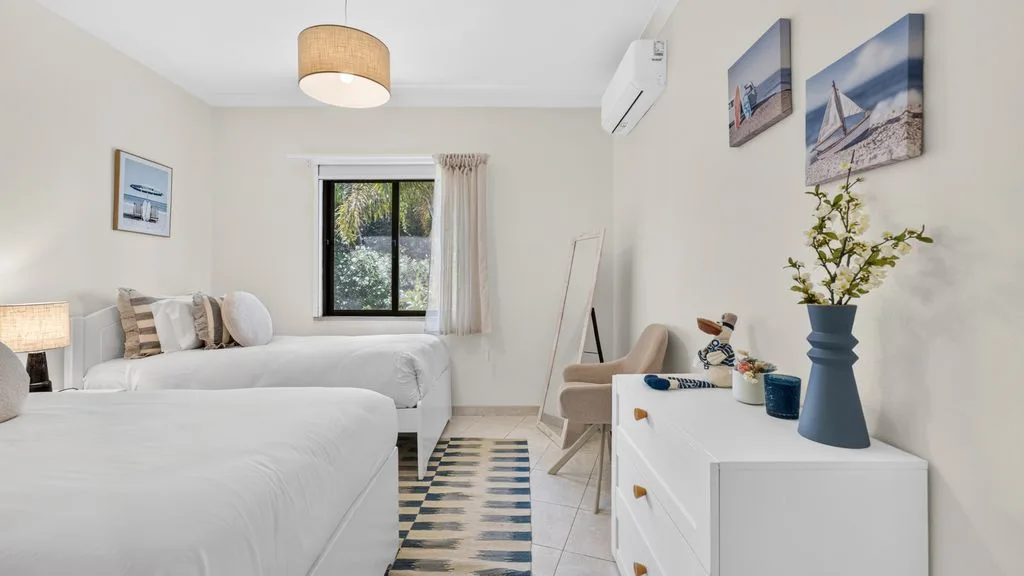 A bright bedroom with beds, a window, and a white dresser.