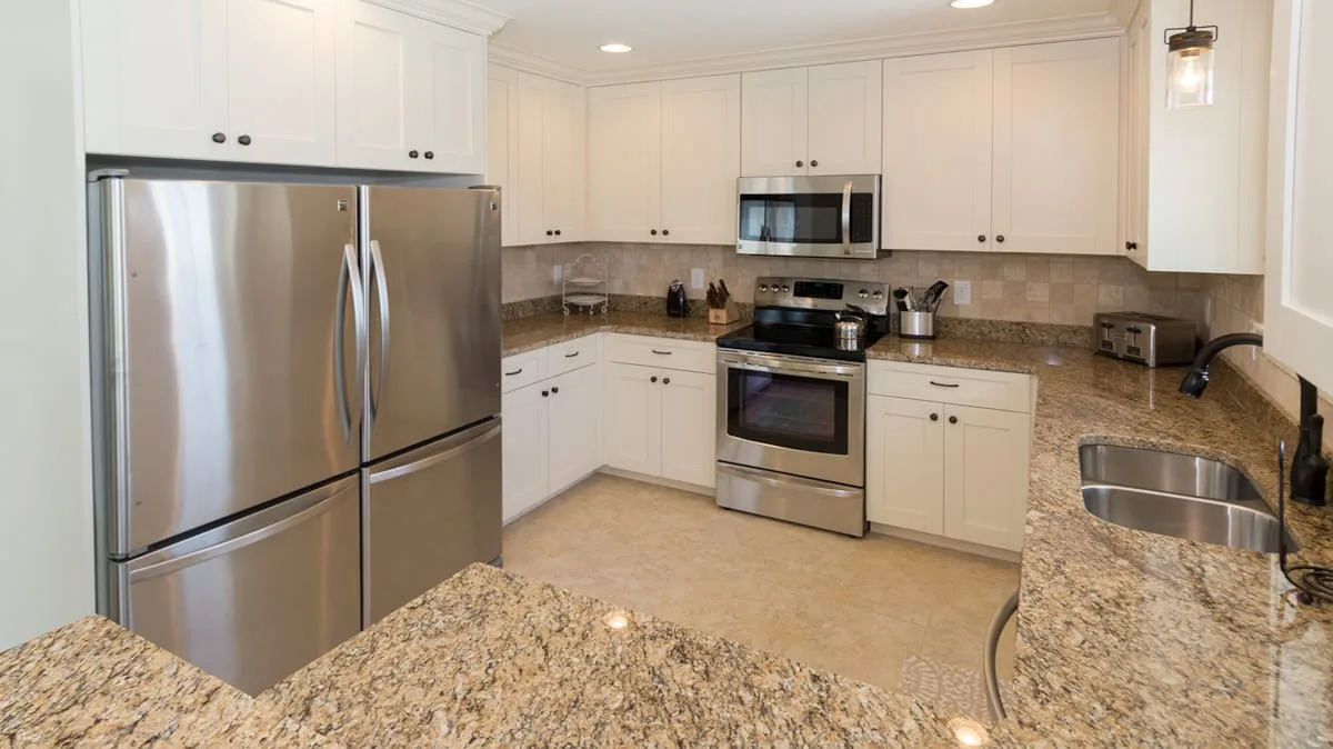 Una cocina luminosa con gabinetes blancos, electrodomésticos de acero inoxidable y encimeras de granito.