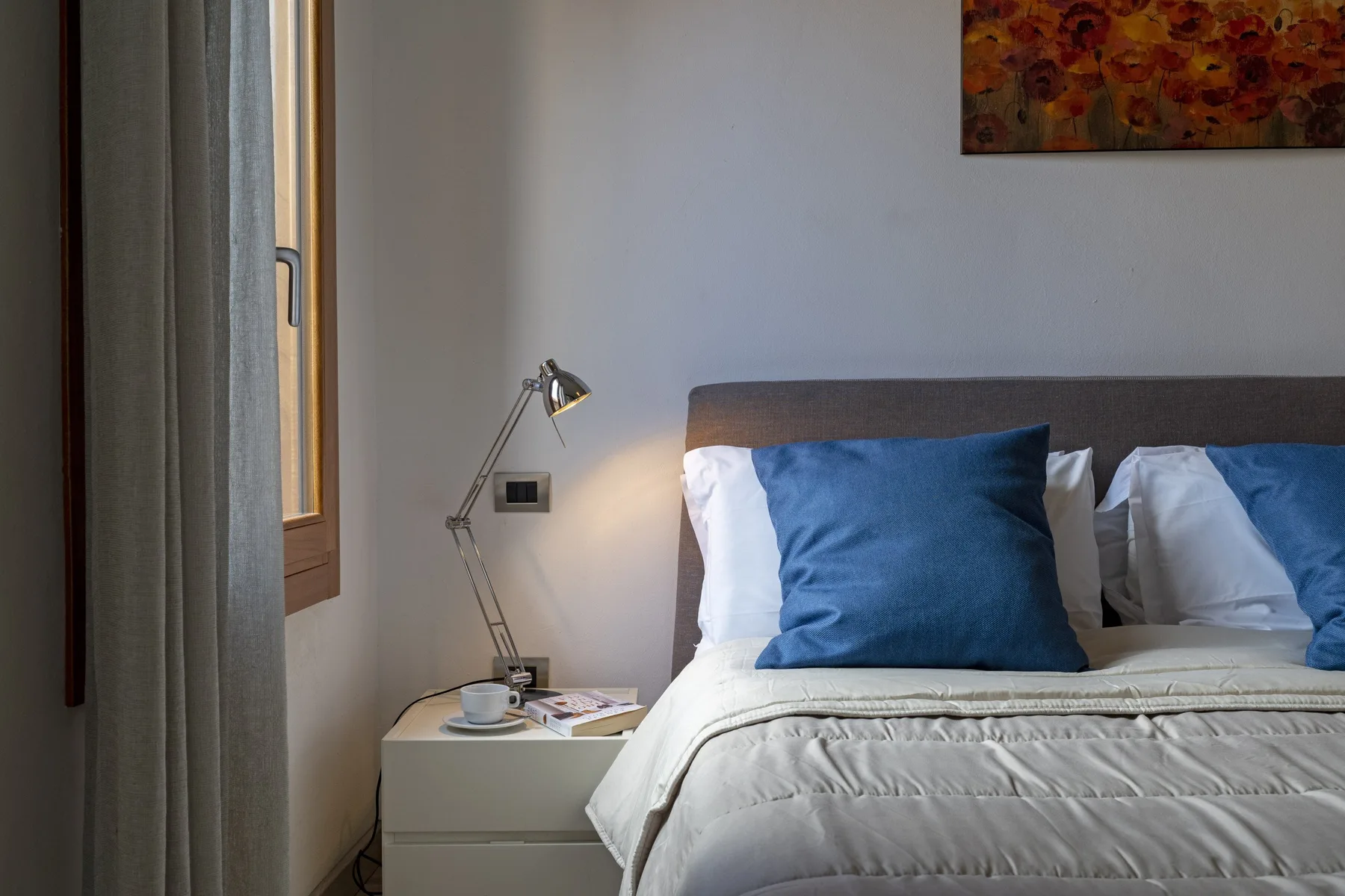 A bedroom with a bed, blue pillows, and a bedside table.