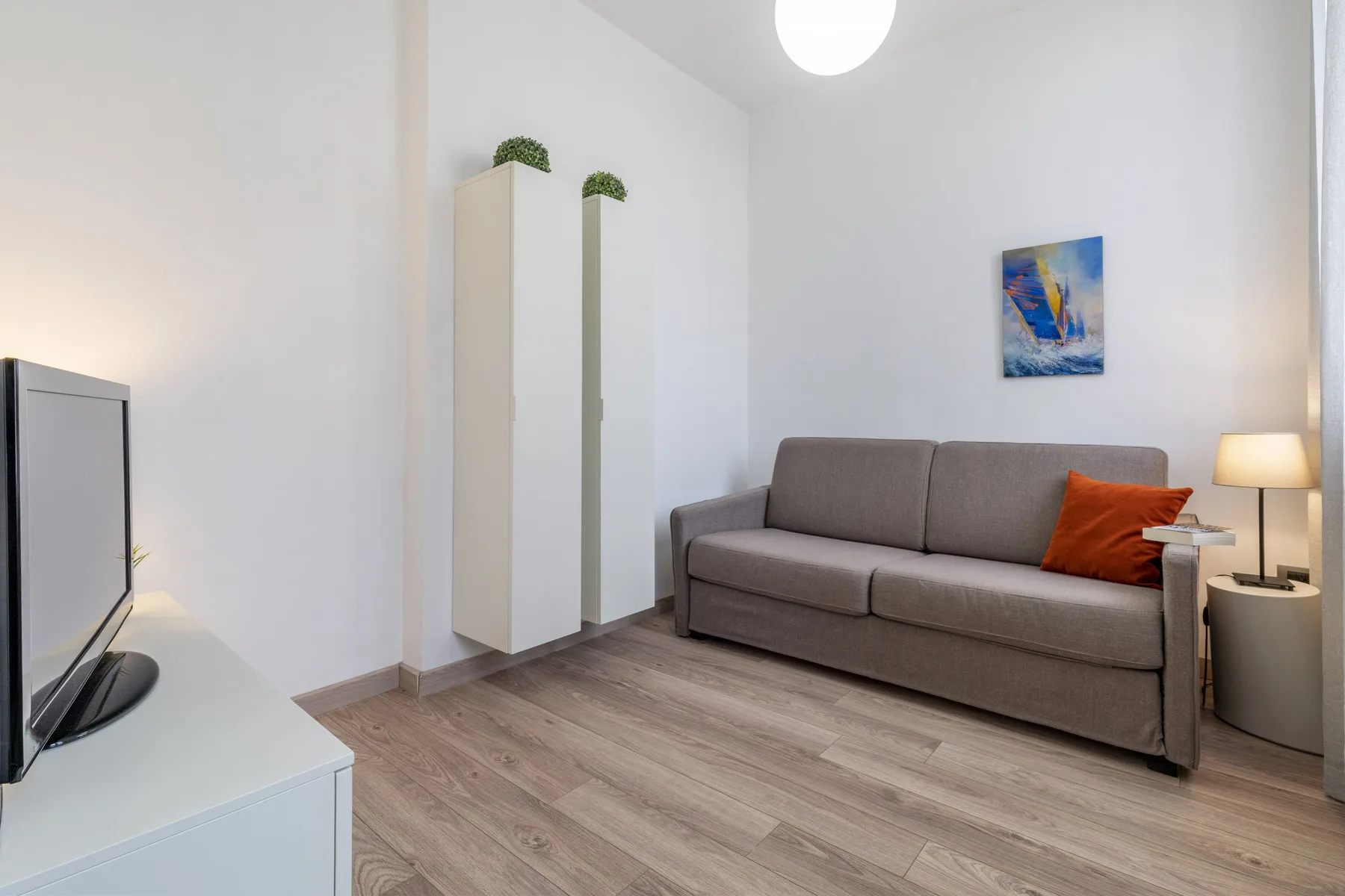 A living room with a gray sofa and a small colorful painting on the wall.