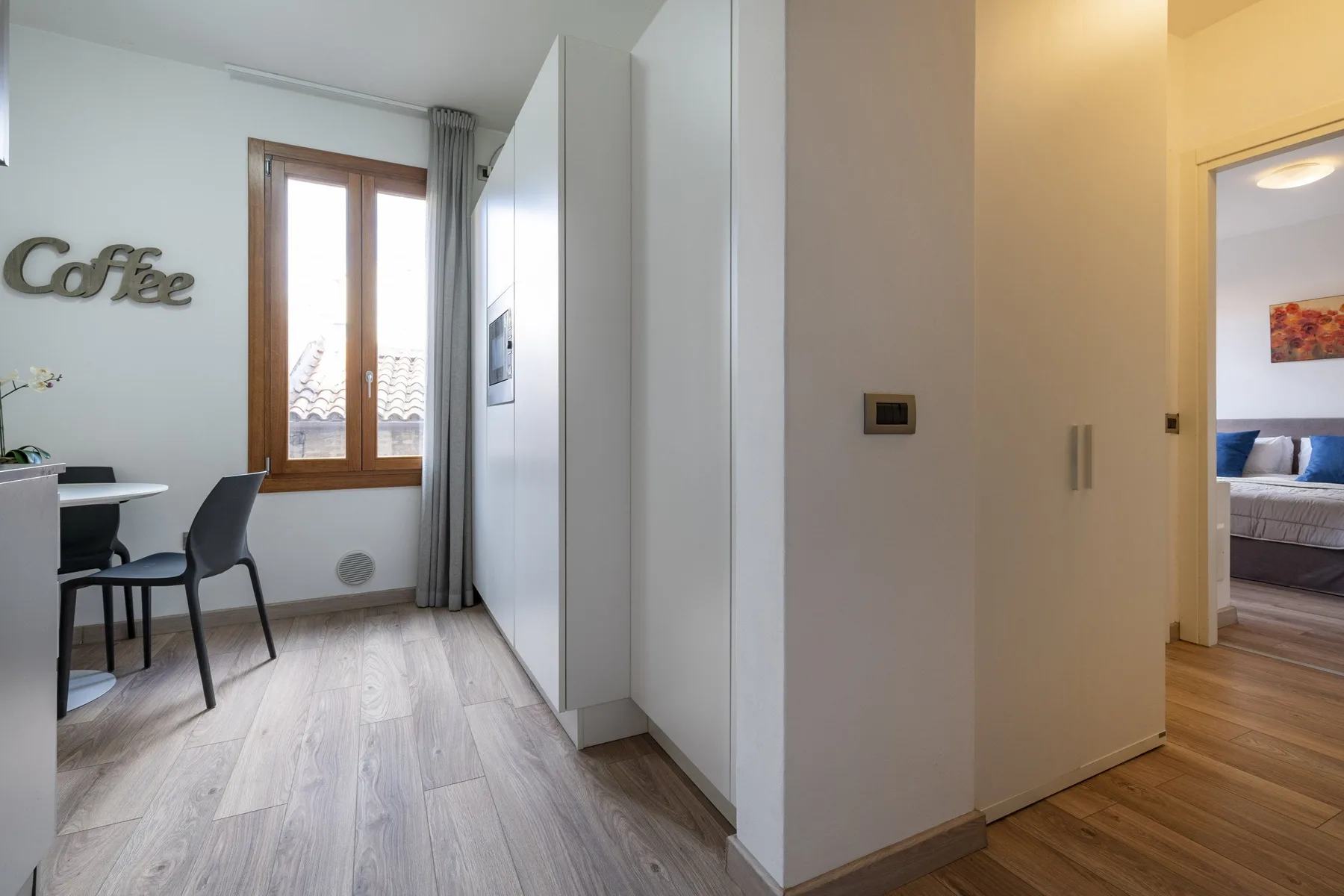 A bright interior hallway connects a small dining area with a bedroom.