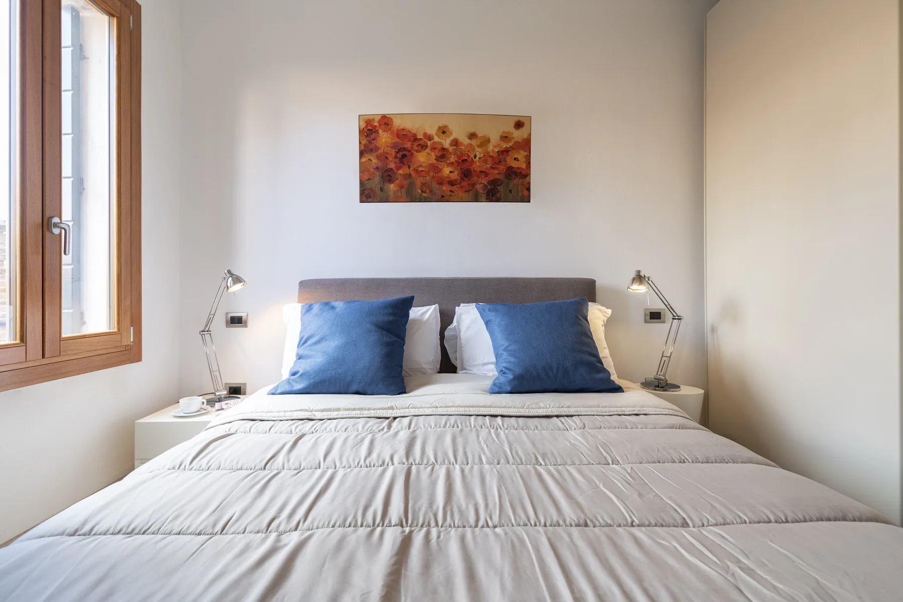 A bedroom with a neatly made bed, blue pillows, and artwork above the headboard.