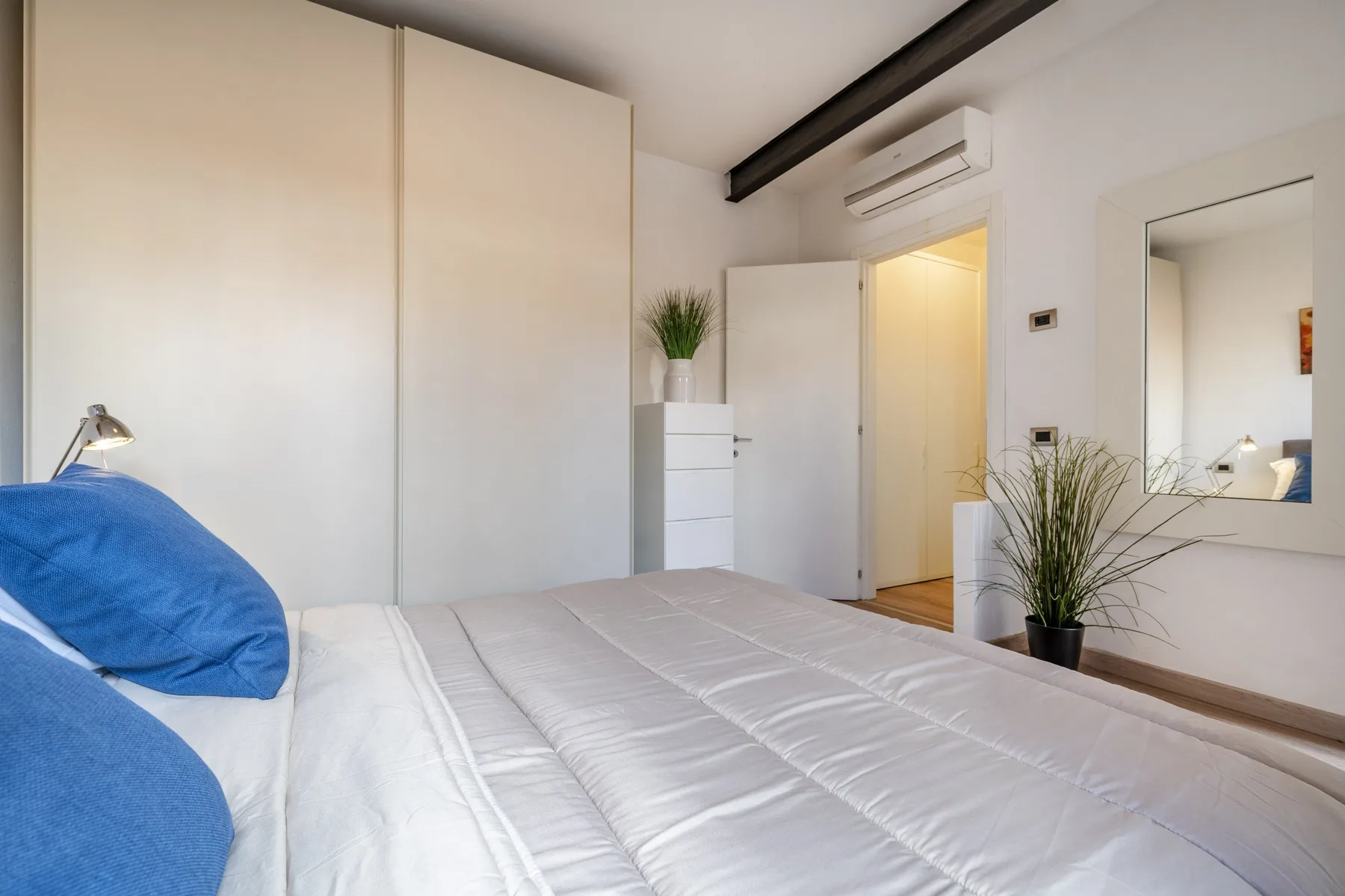 A bright bedroom with a bed, blue pillows, and a potted plant.