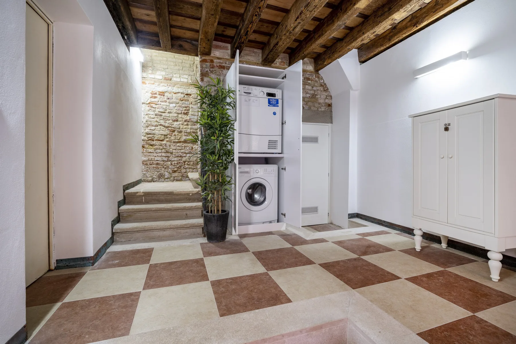 A laundry area with a washing machine beneath exposed wooden ceiling beams.
