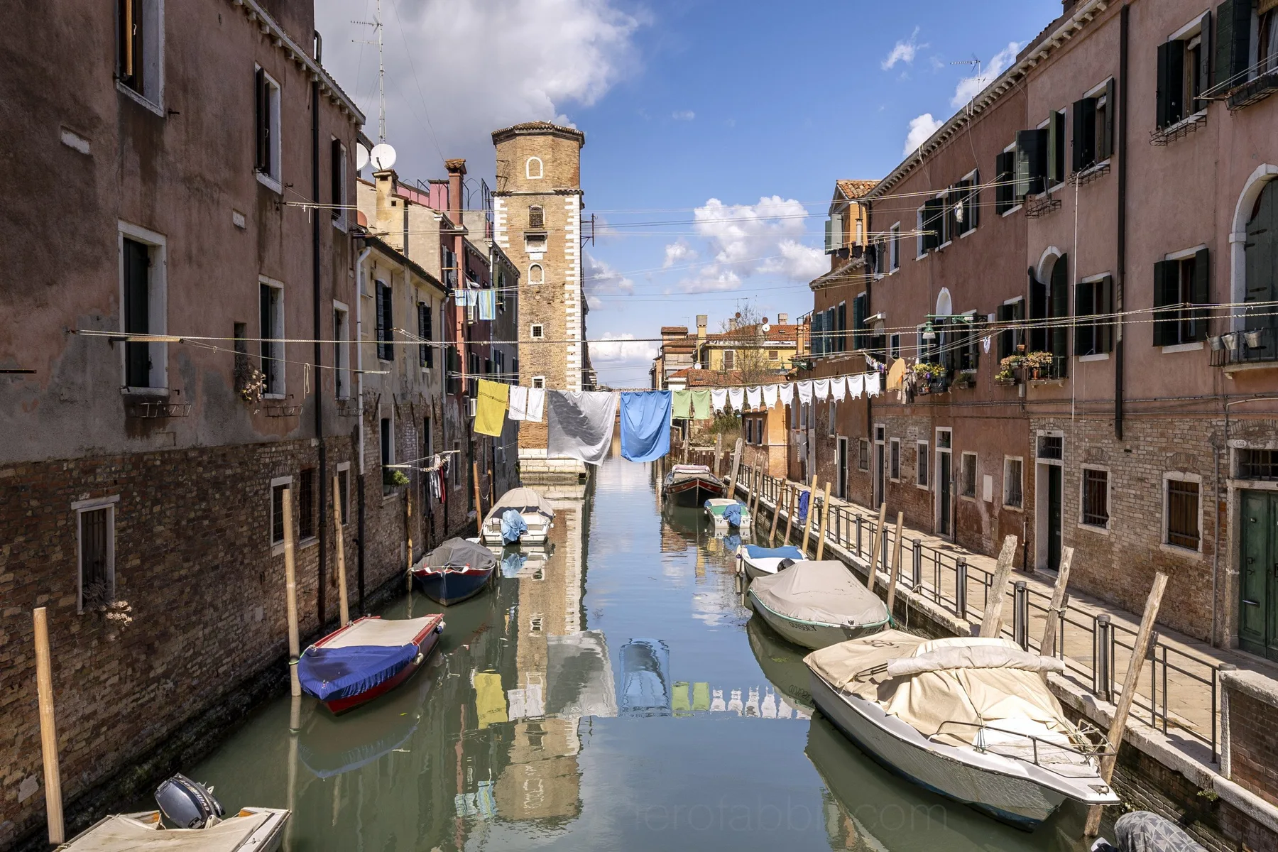 A narrow canal runs between closely spaced buildings, with boats moored along the banks.