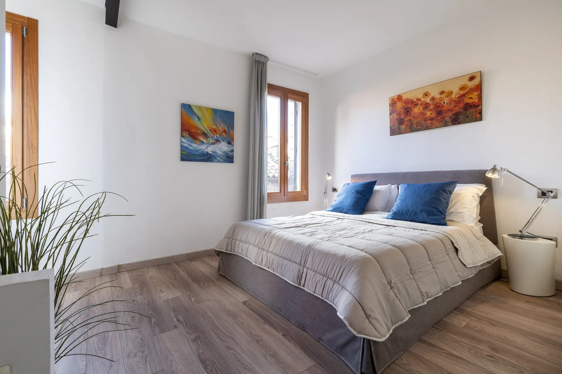 A bright bedroom with a neatly made bed and colorful artwork on the walls.