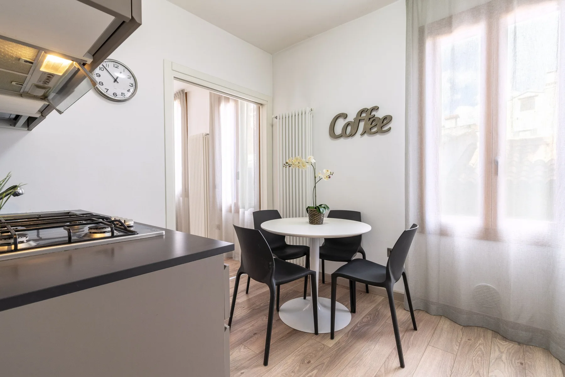 A bright kitchen dining area with a round table and dark seating.