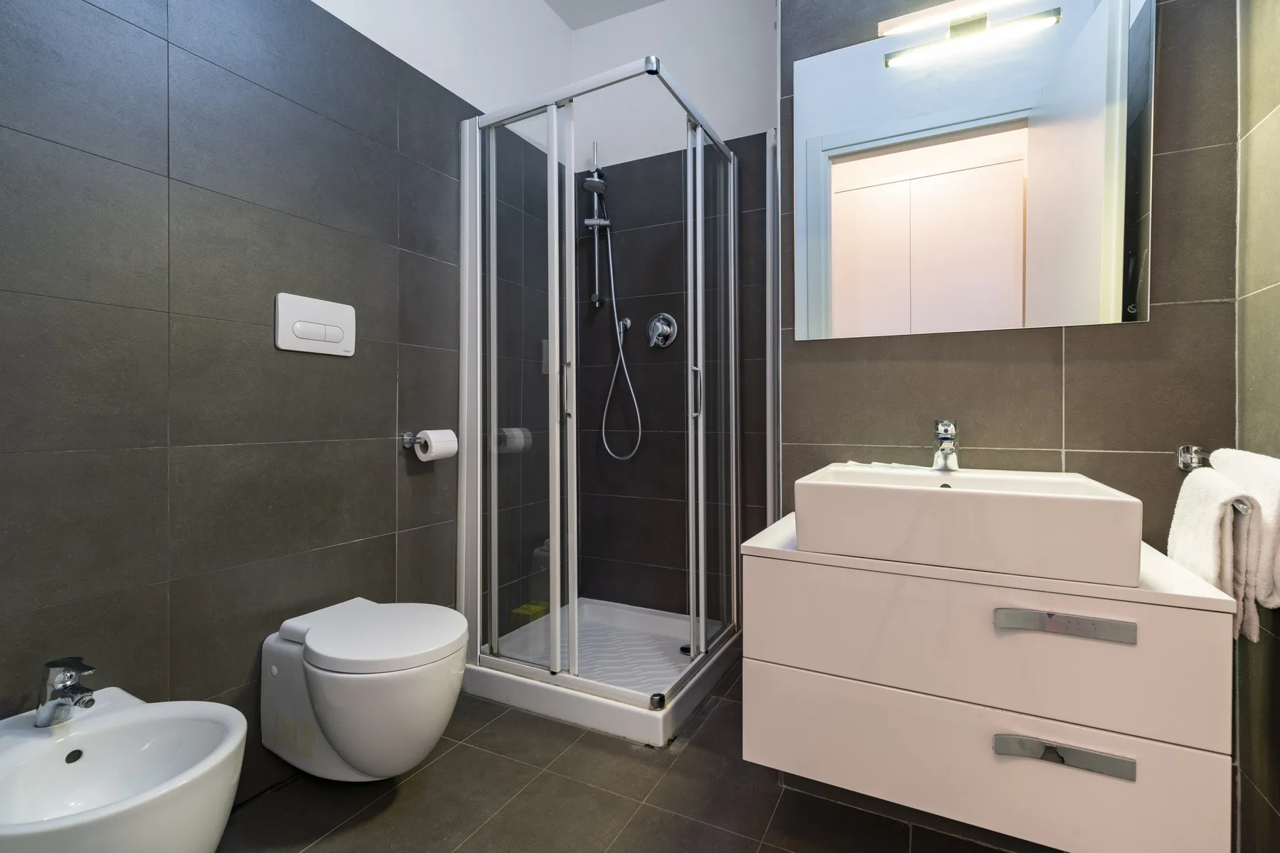 A modern bathroom with a glass shower, wall-mounted toilet, and sink vanity.