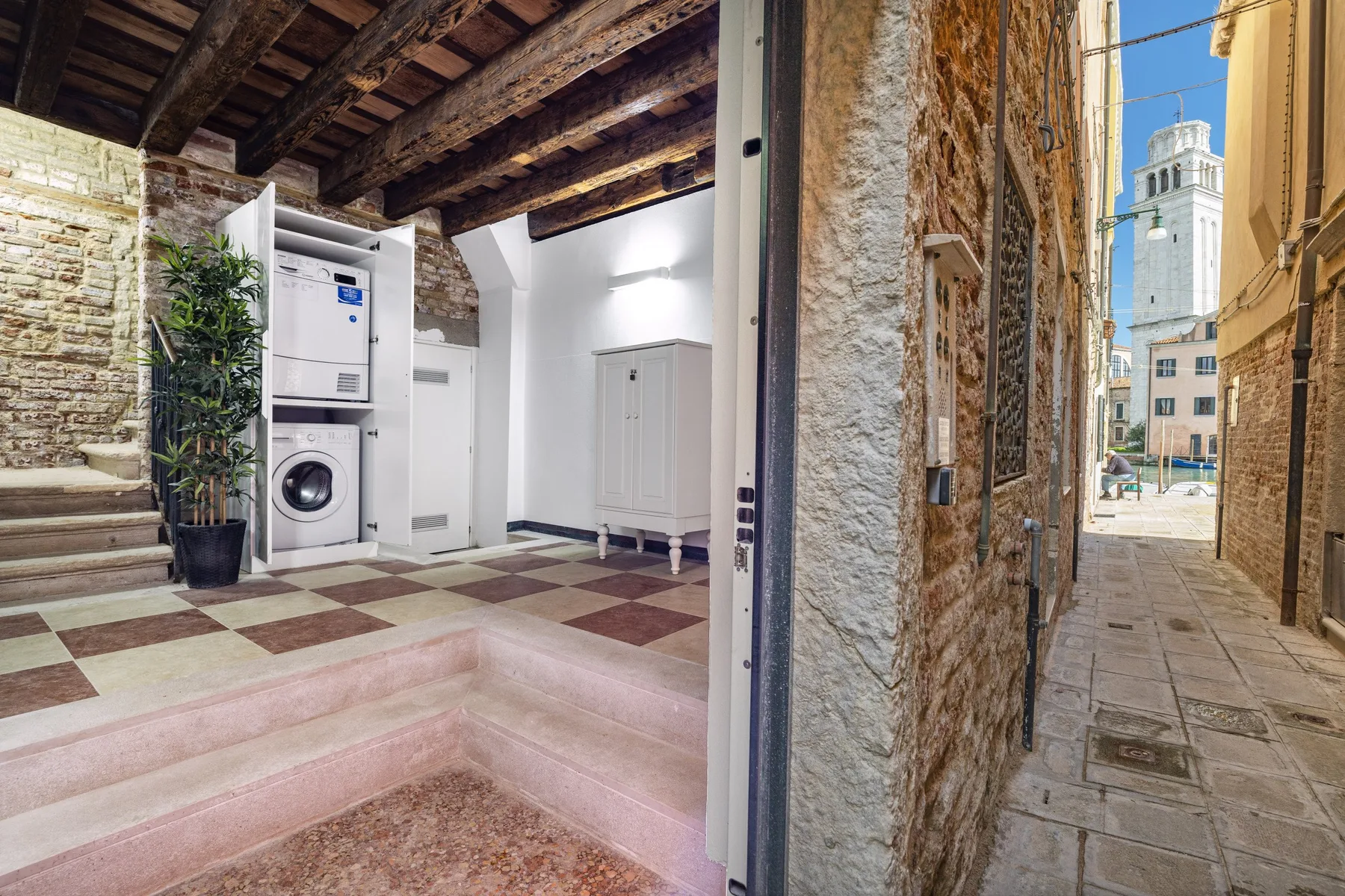 A laundry area with washing machines and a narrow stone-paved passage outside.