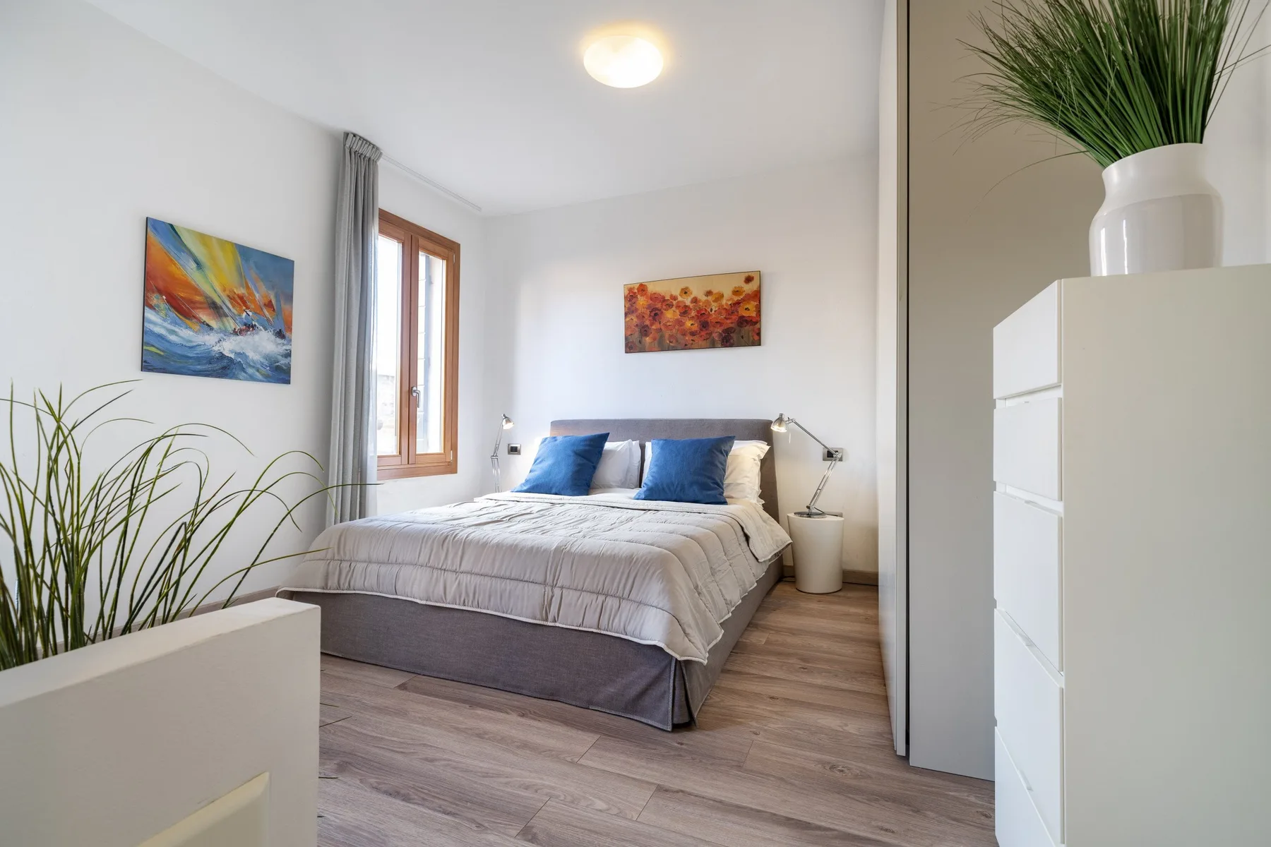 A bright bedroom with a bed, colorful wall art, and a potted plant.