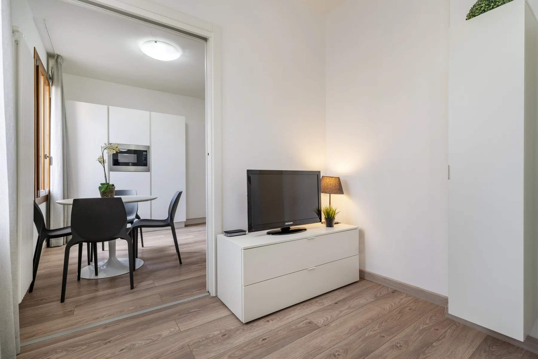 A bright living area with a television and dining space visible through an open doorway.