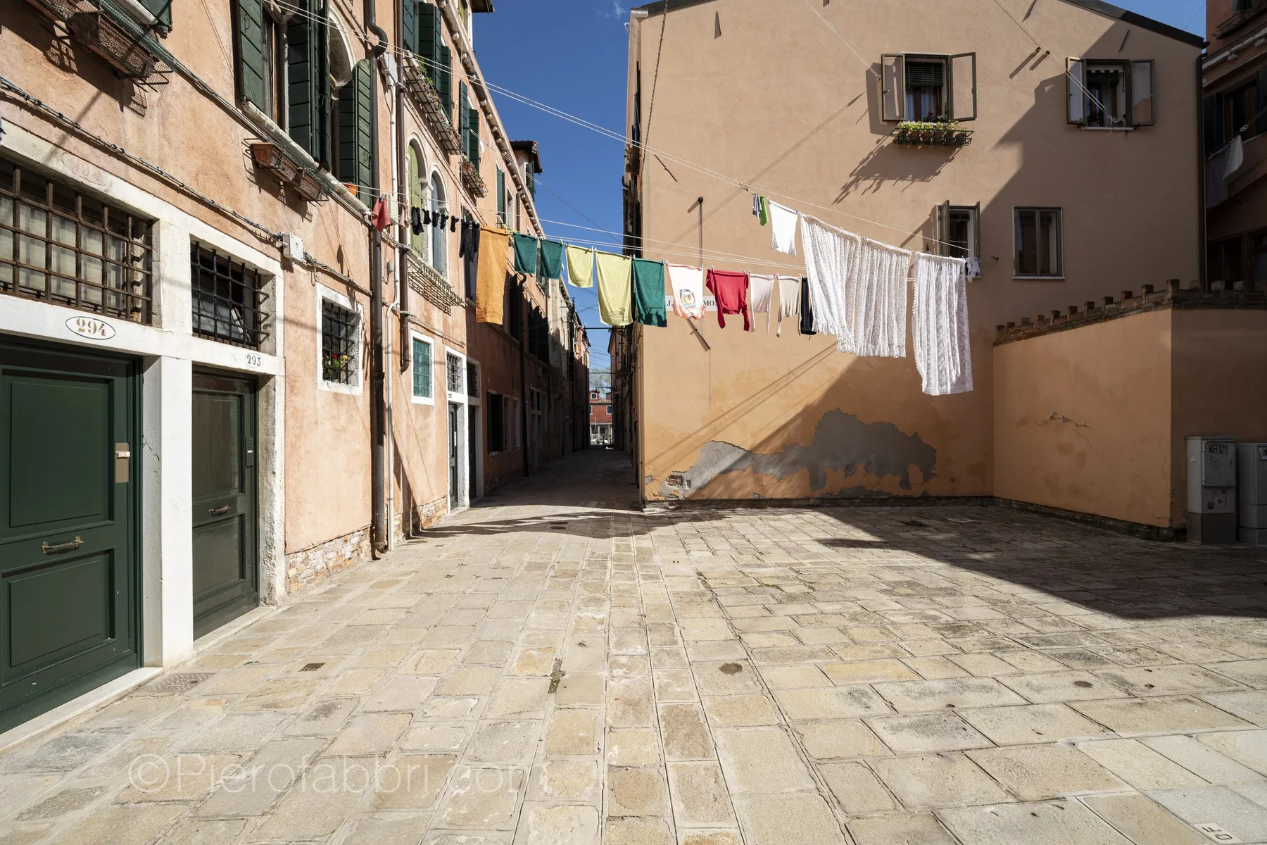 A sunlit paved courtyard between buildings, with laundry hanging overhead.