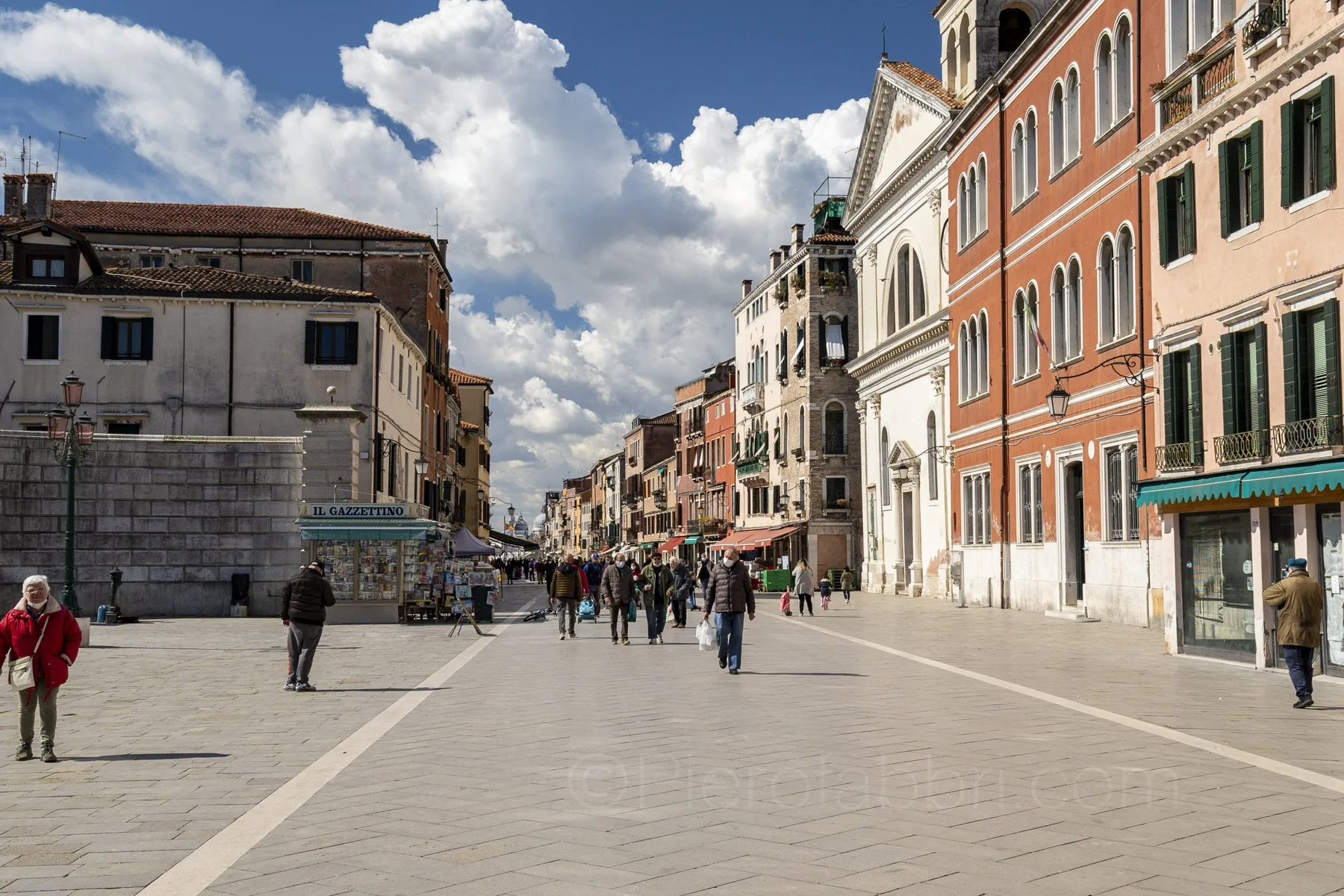 A broad pedestrian street runs between historic buildings under a cloudy sky.