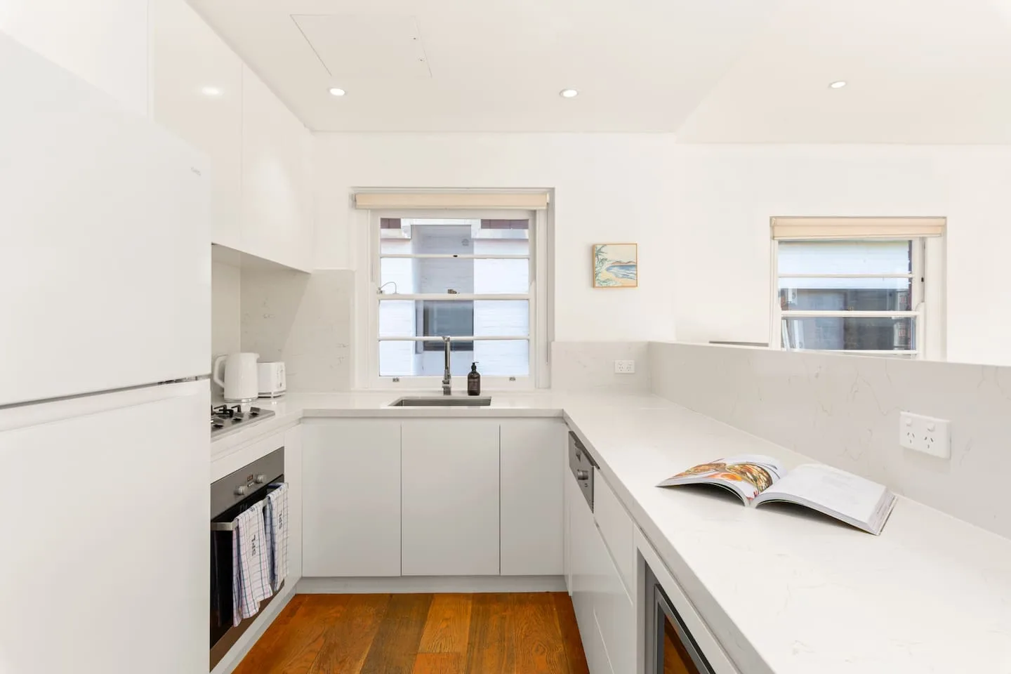 A bright kitchen with white counters and an open book on the counter.