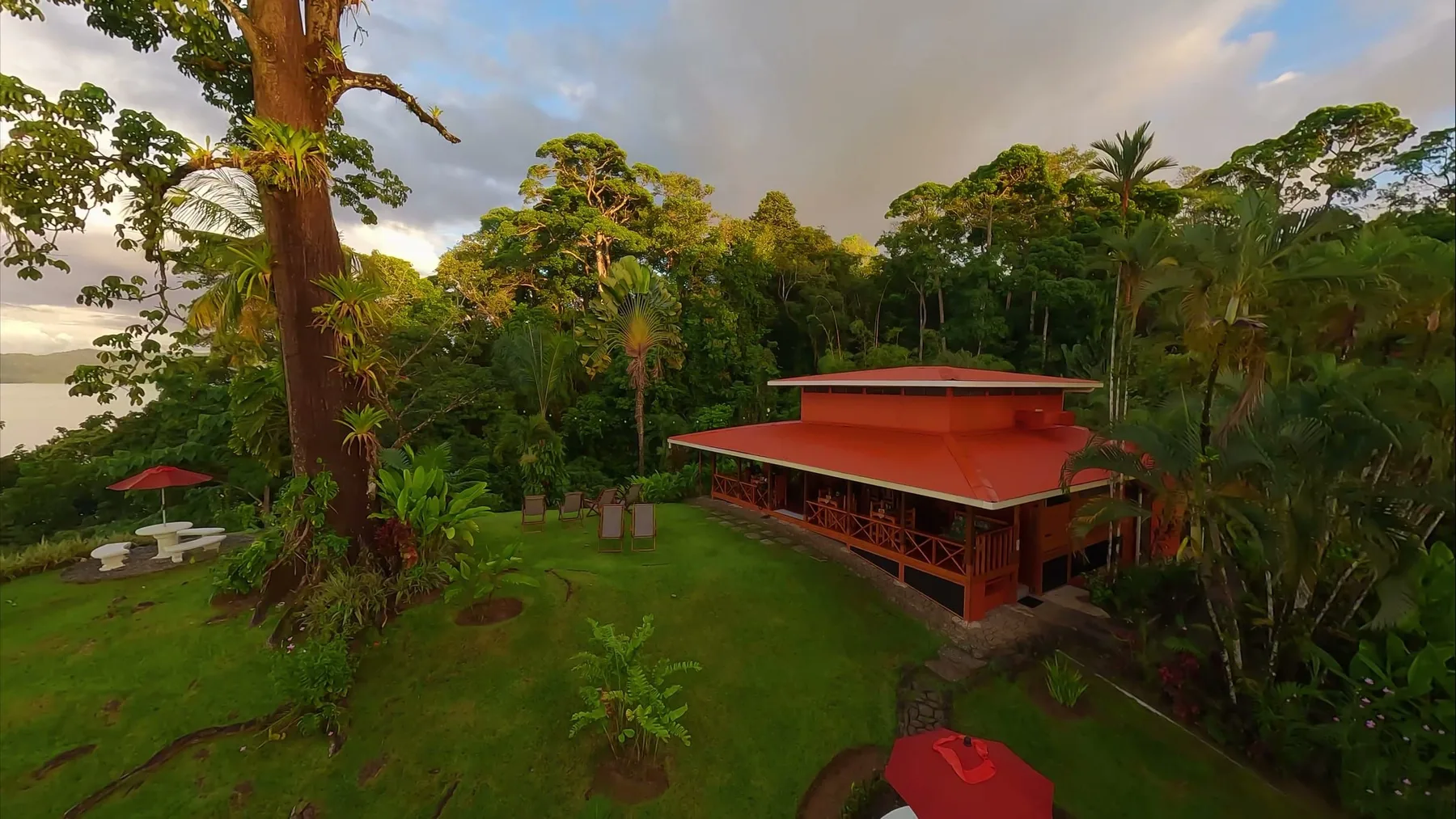 The lodge's red-roofed main house and garden in the rainforest, with the sea beyond