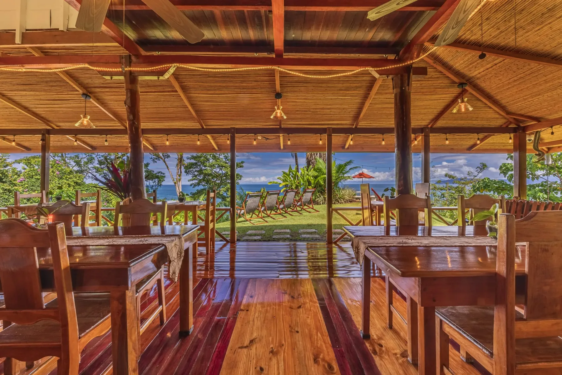 The open-air restaurant with wooden tables, looking out over the lawn to the Pacific